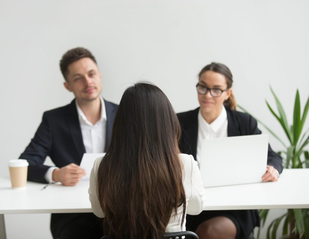 Back close up view of female applicant being interviewed by two HR managers reading her resume, checking data on laptop, asking questions for job position. Employment, hiring, first impression concept